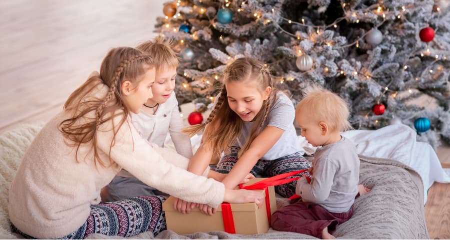 Children opening a present in the family room beside a Christmas tree.
